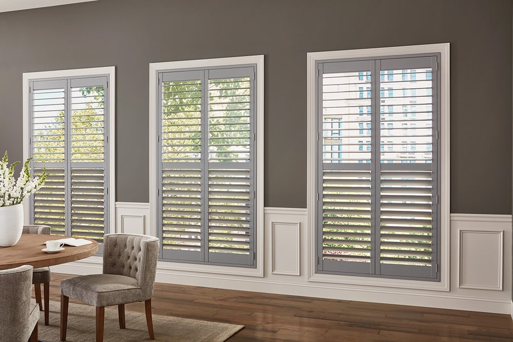 Gray composite shutters filtering in light into a modern looking dining room.