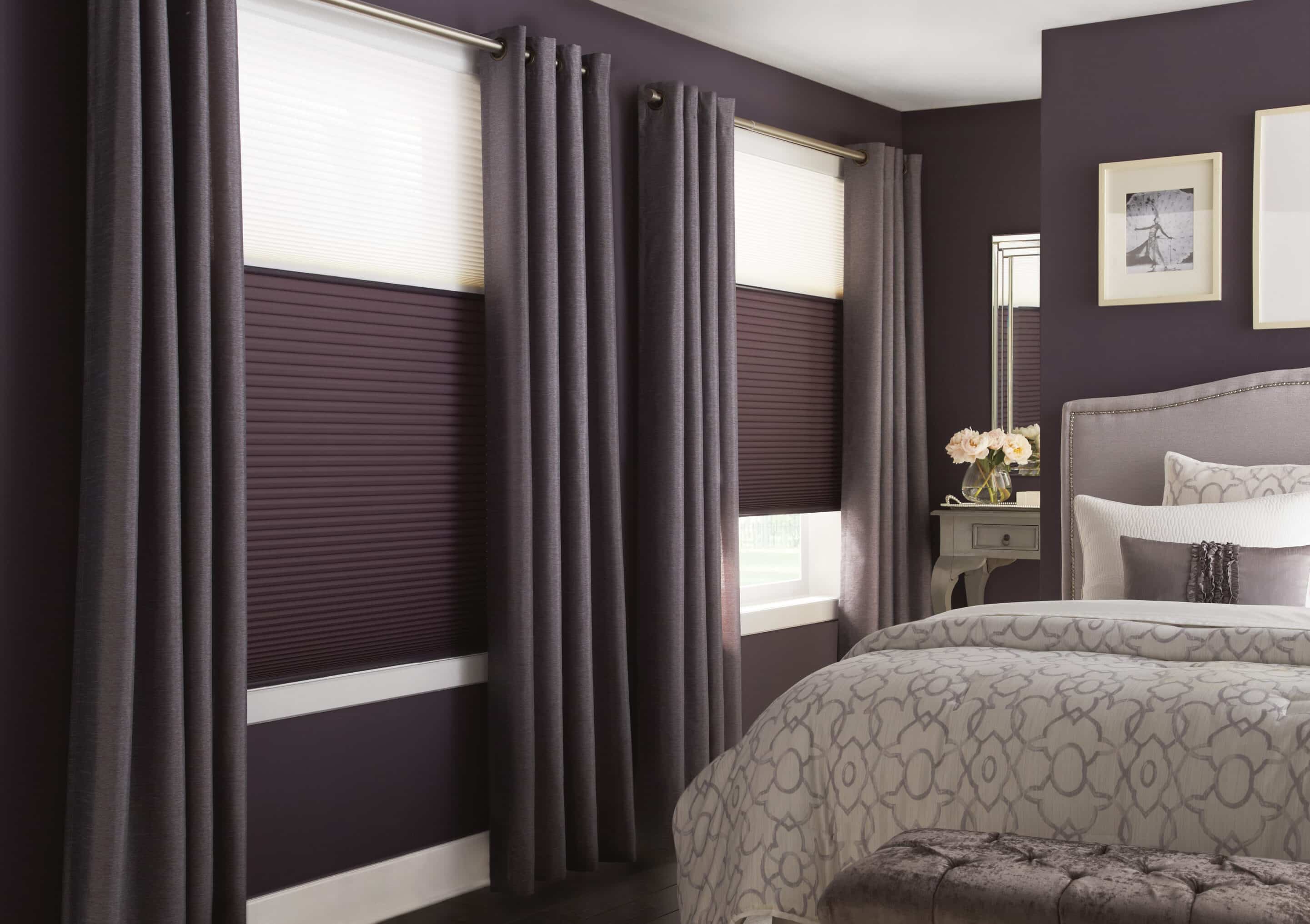 Bedroom with dark purple walls featuring gray floor-length curtains and matching purple cellular shades on two windows.
